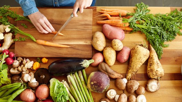 Woman cutting carrots by various vegetables
