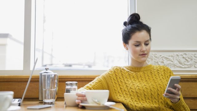 Woman texting and drinking cappuccino in cafe