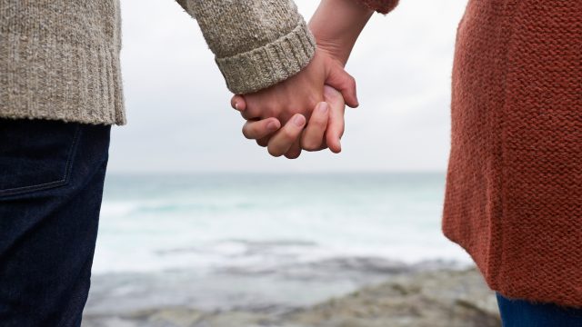 Close up of couple holding hands on coastline.