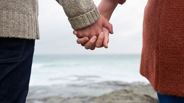 Close up of couple holding hands on coastline.