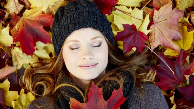 Germany, Hamburg, Woman lying with eyes closed on maple leaves in autumn, close-up