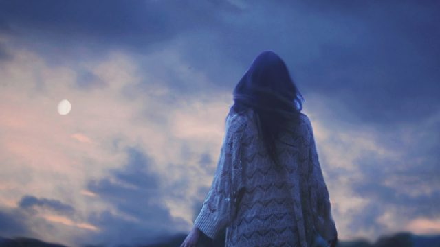 Woman wearing sweater walking outdoors at dusk under visible moon