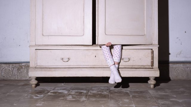 Girl (8-9) sitting inside wardrobe with door closed, low section