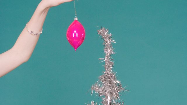 Woman putting Christmas decoration on artificial tree, close-up