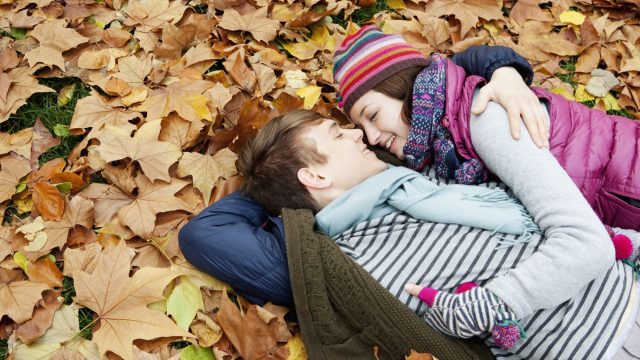 couple hugging,laying in autumnleaves in park.