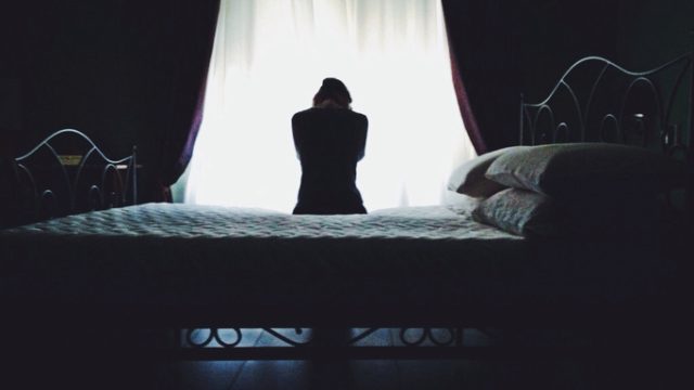 Rear View Of Woman Sitting On Bed Against Curtain
