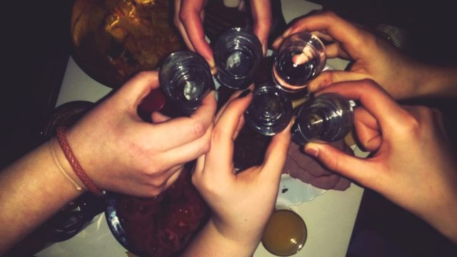 Close-Up Of Hands Toasting Shot Glasses In Restaurant