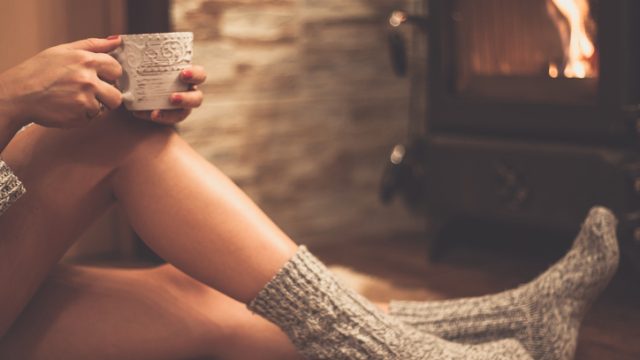 Woman sitting  in front of a wood burning stove with mug of tea