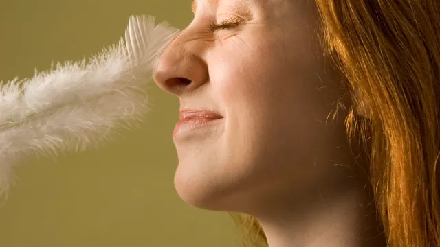 Young woman with nose being tickled by feather, profile