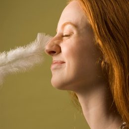 Young woman with nose being tickled by feather, profile