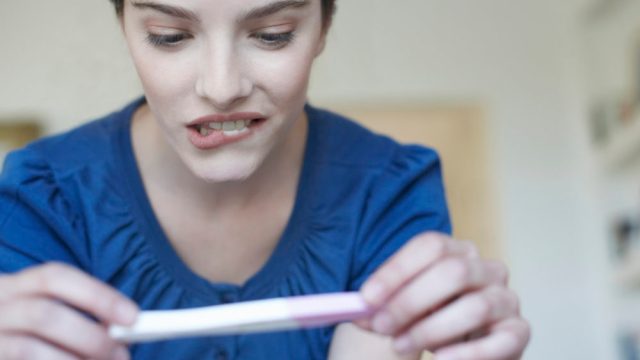 Woman holding home pregnancy test and looking worried
