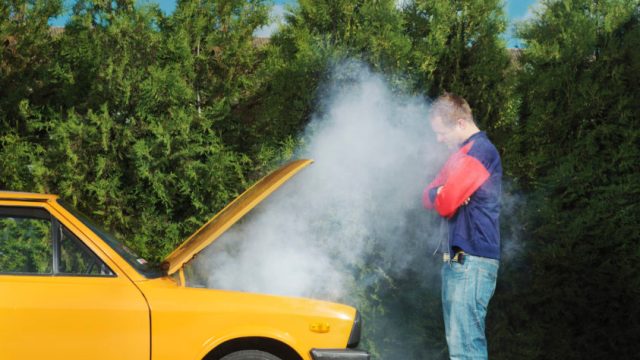 Man looking at yellow car with steam pouring from bonnet