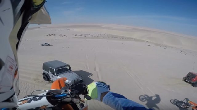 dirt biker jumps off sand dune into jeep