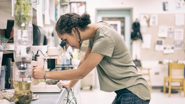 Teenage girl looking through microscope in science classroom