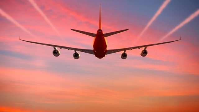 Airplane flying in the sky at sunset with vapor trails