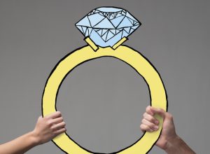 Two hands holding up a large illustrated engagement ring