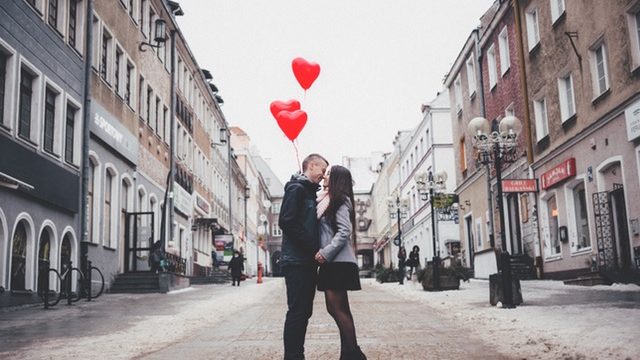 A couple kissing while holding heart balloons