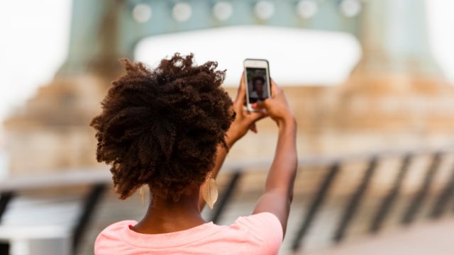 Woman with afro taking selfie on iPhone.