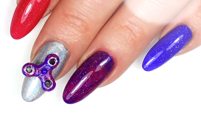 Hand with painted acrylic nails with a nail-sized fidget spinner