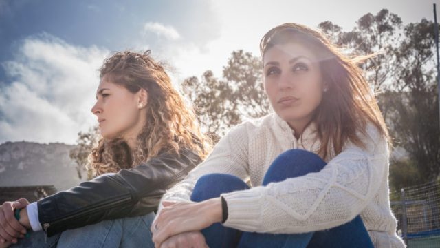 Two sullen young women friends sitting on breezy beach