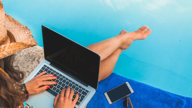 Woman sitting by the pool working on a laptop.