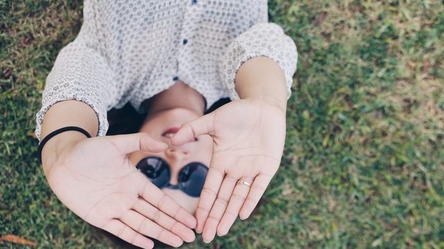 Woman lying on grass raising her hands into a heart