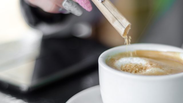 Female hand pours sugar in coffee