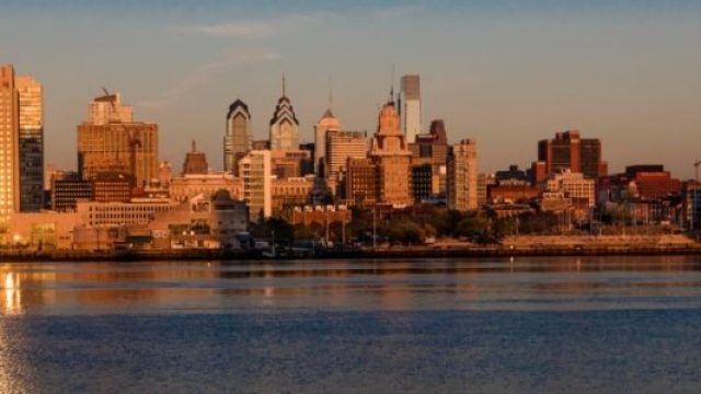 Philadelphia, PA skyscrapers and skyline at sunrise reflect golden light in Delaware River,