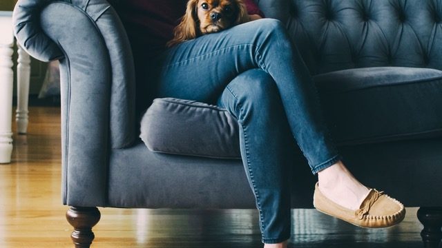 Woman sits on couch with dog in lap