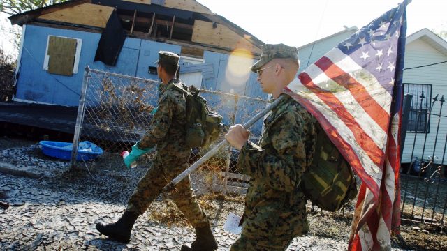 UNITED STATES - CIRCA 2002: Cpl. Karl Krebsbach carries a tattered and muddied American flag he found as he and other Marines from Camp Lejeune, N.C., patrol a Lower Ninth Ward neighborhood for a second time to search for signs of life in the aftermath of Hurricane Katrina. (Photo by Linda Rosier/NY Daily News Archive via Getty Images)
