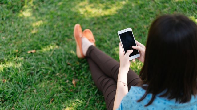 Woman sitting on the grass using her phone.