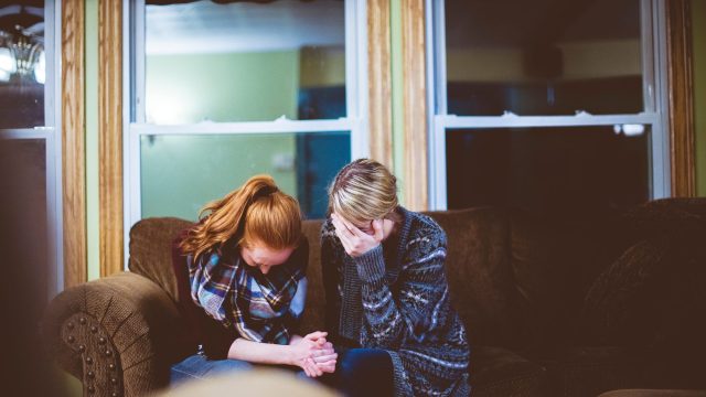 two friends sit on a couch holding hands