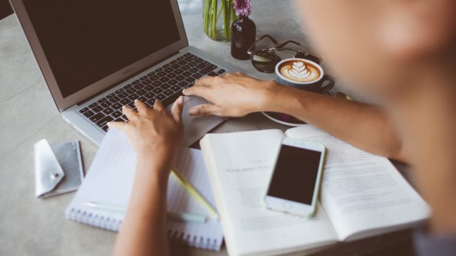 person typing on laptop with cellphone on open book