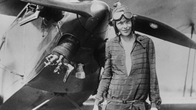 Black and white photo of Amelia Earhart standing in front of her bi-plane called "Friendship" in 1928.