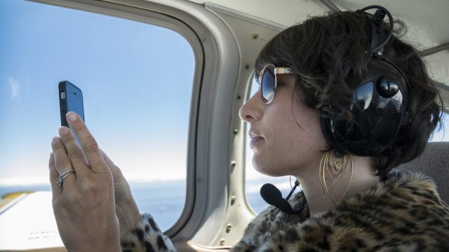 A woman takes a photo with her cell phone during a private flight on a small airplane.