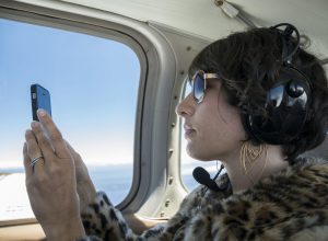 A woman takes a photo with her cell phone during a private flight on a small airplane.