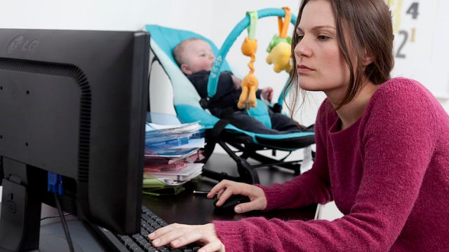 Mom on the computer with her baby in the background