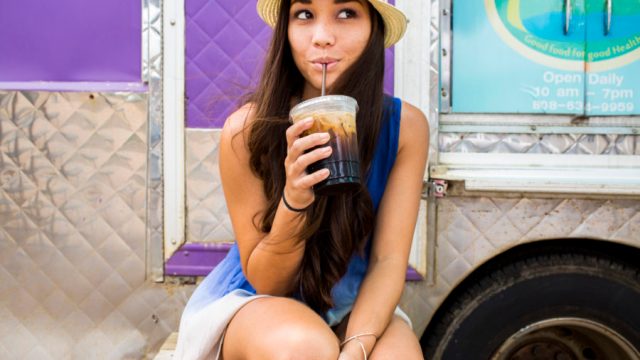 Woman drinking ice coffee near food cart