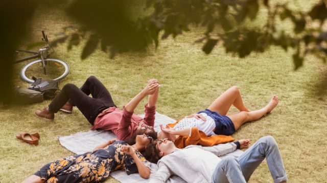Friends taking selfie laying in circle on blanket in park