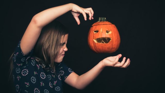 A girl concentrates with all her strength as she levitates a jack-o'-lantern.