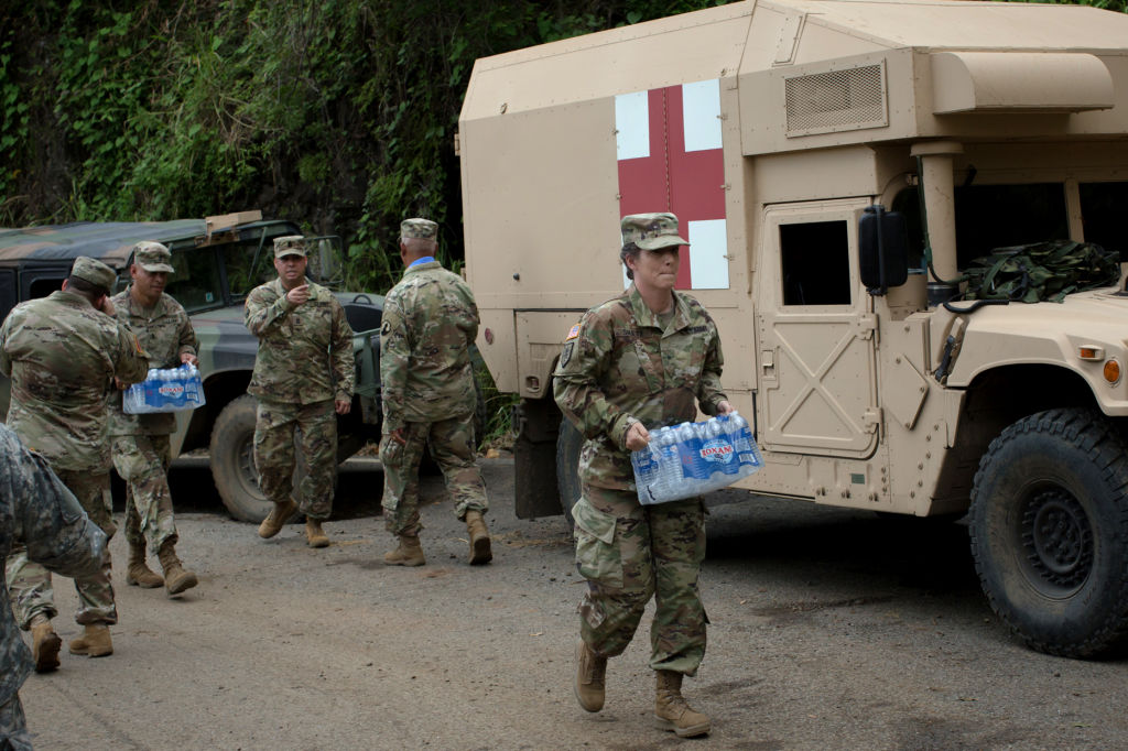 Soldiers assigned to the 1st Mission Support Command, U.S. Army Reserve, move cases of bottled water while working to clear roads of debris near Adjuntas, Puerto Rico, on Saturday, Oct. 7, 2017. U.S. lawmakers pledged to back Puerto Rico's recovery as Governor Ricardo Rossello prepares to ask Congress for a multibillion-dollar aid package to help rebuild from the devastation caused by Hurricane Maria. Photographer: Alex Flynn/Bloomberg via Getty Images