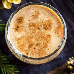 Eggnog with cinnamon in glass close up with Christmas decor - homemade traditional festive drink for Christmas time
