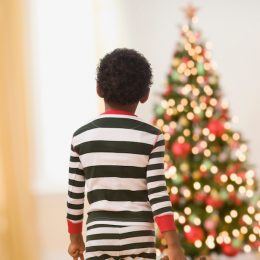 African boy in pajamas with teddy bear looking at Christmas tree