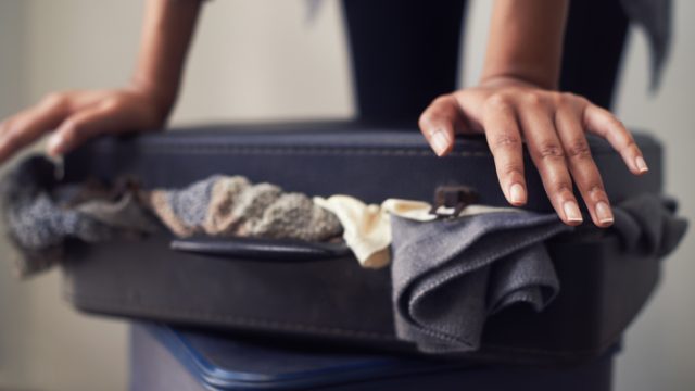A woman trying to close an over-full suitcase