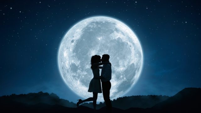 Silhouette of loving couple kissing against the full moon