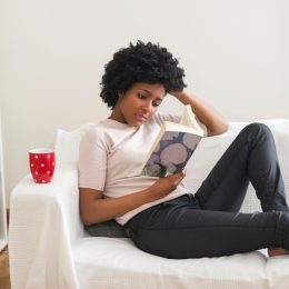 Black woman reading book on sofa