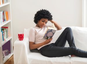 Black woman reading book on sofa