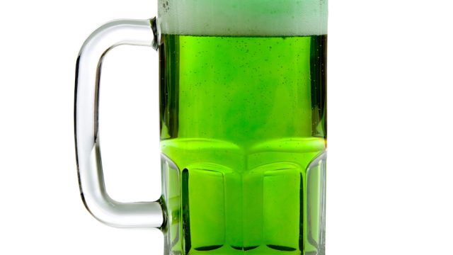A beer mug of green beer with a foamy head on a white background - St. Patricks Day themd