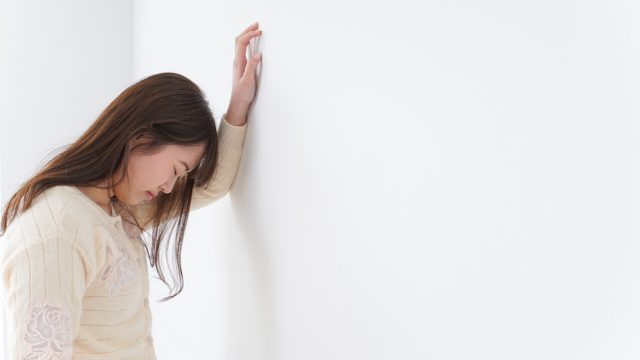 Young woman leaning against wall suffering from illness