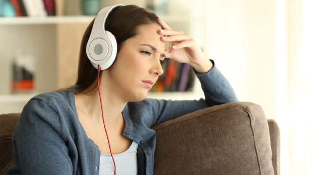 Worried girl listening to music sitting on a couch in the living room at home